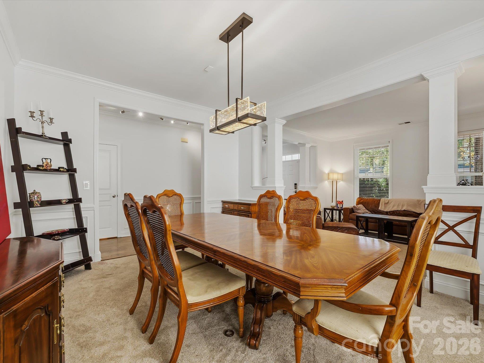 A spacious formal dining room features elegant crown molding, architectural columns, and a contemporary statement light fixture, creating an inviting setting for gatherings and entertaining. - 11732 Windy Mist Way, Huntersville