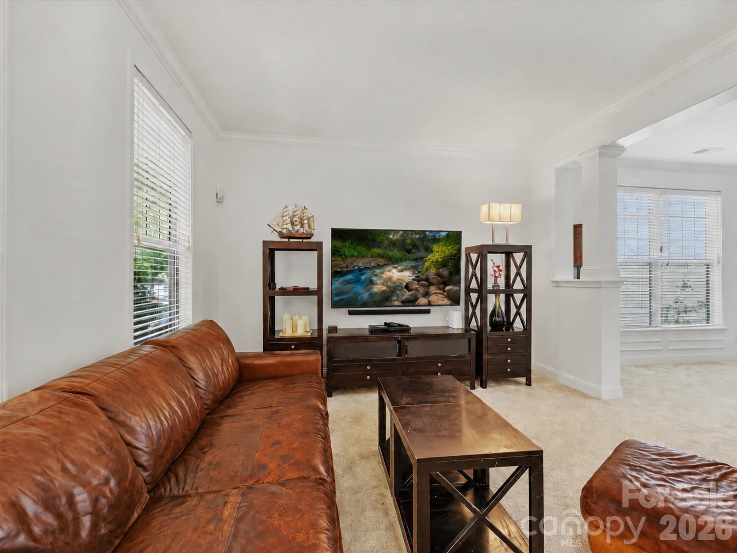 A spacious living room features abundant natural light, elegant crown molding, and an open connection to the dining area for comfortable everyday living and entertaining. - 11732 Windy Mist Way, Huntersville