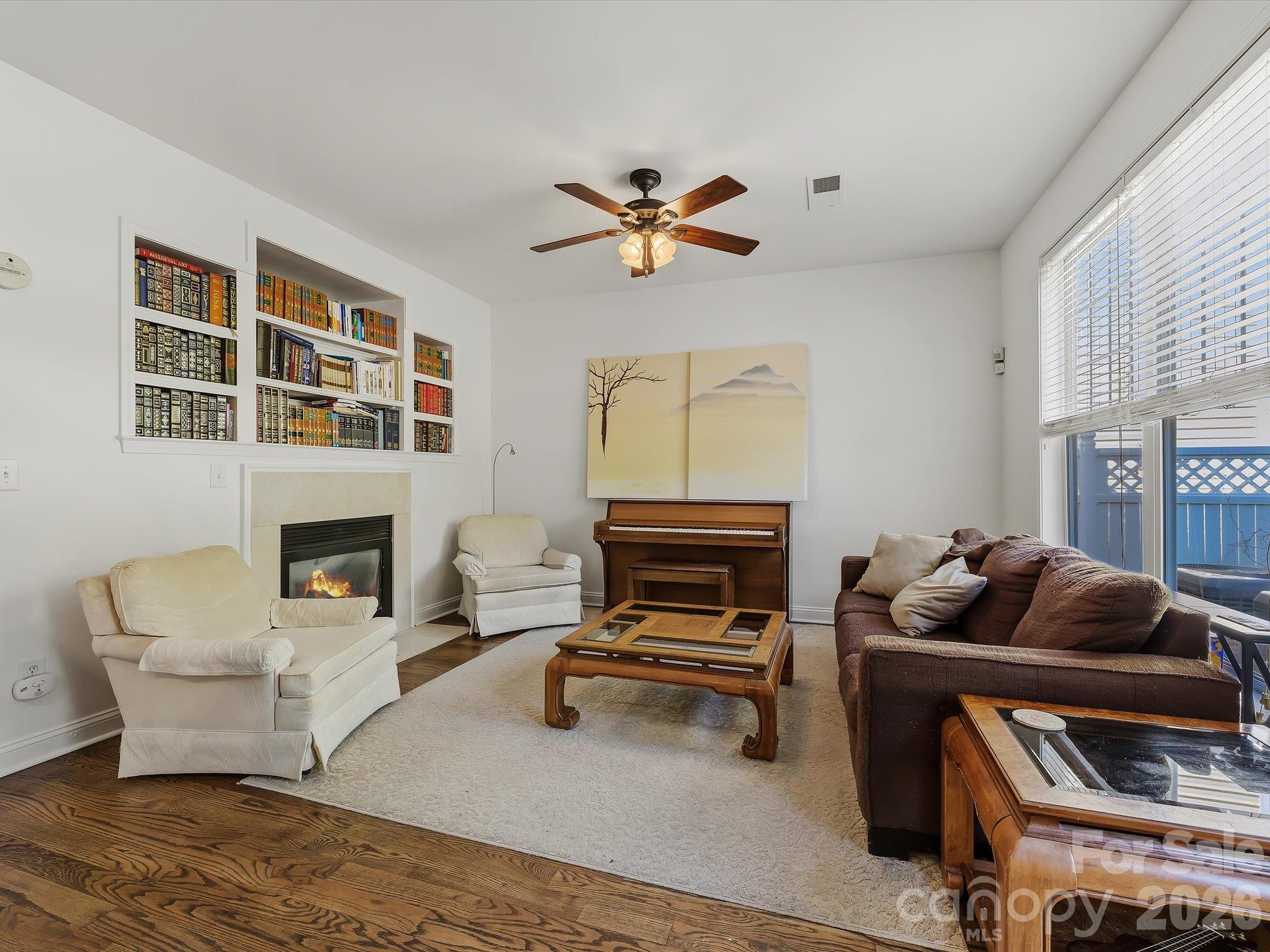 A bright great room features a cozy fireplace (in "as is" condition) with built-in shelving, hardwood floors, and abundant natural light for comfortable everyday living. - 11732 Windy Mist Way, Huntersville