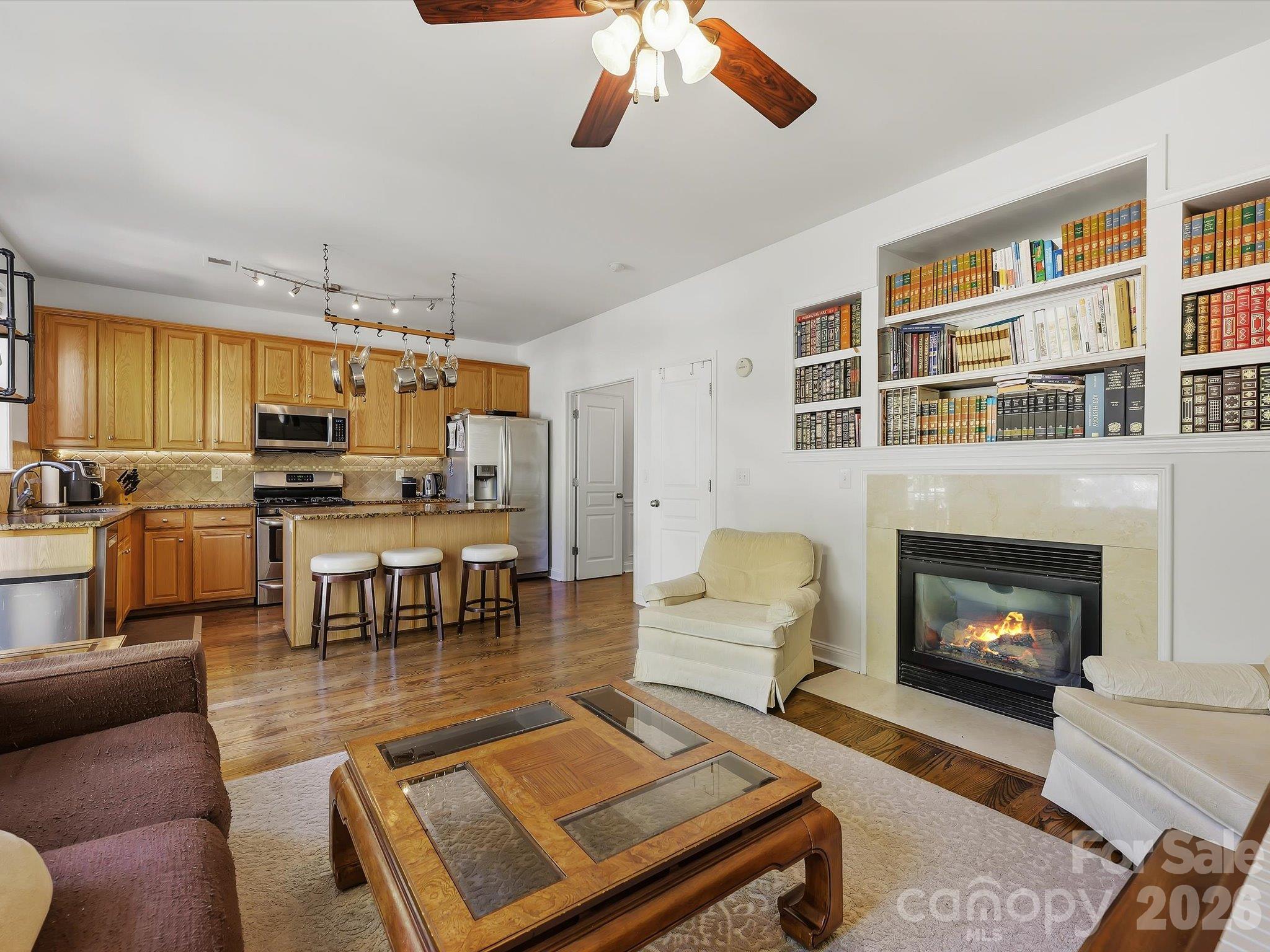 The open-concept great room flows seamlessly into the kitchen, featuring hardwood floors, a cozy fireplace (in "as is" condition) with built-in shelving, abundant natural light, and a breakfast bar for casual seating. - 11732 Windy Mist Way, Huntersville