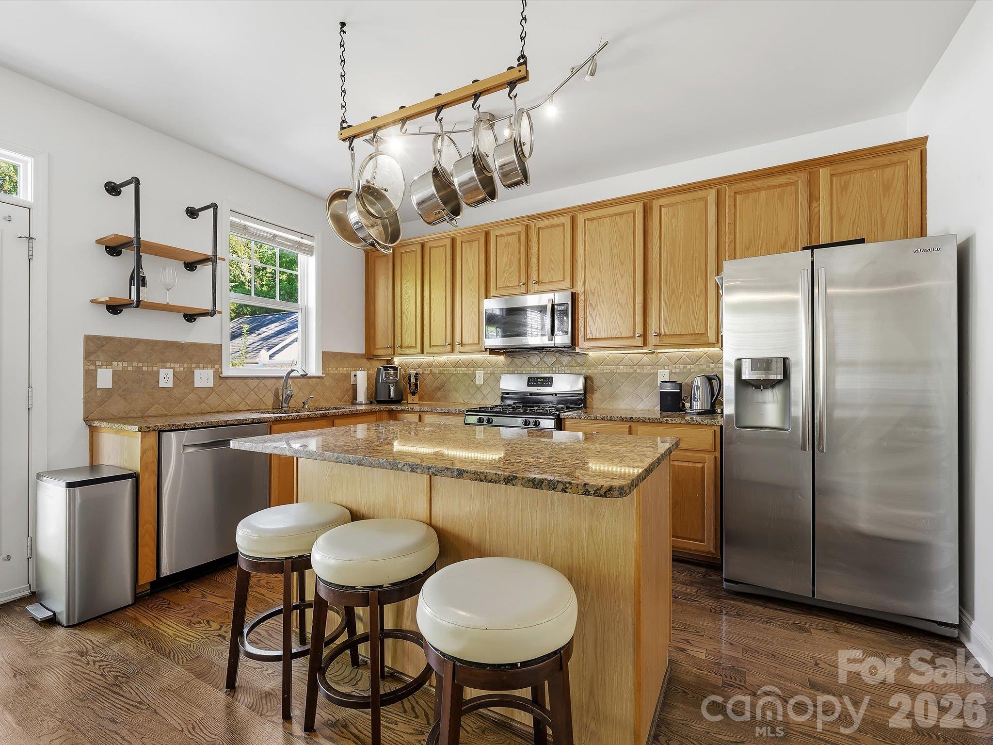 The spacious kitchen features abundant cabinetry, granite countertops, stainless steel appliances, a tile backsplash, and a large center island with casual seating. - 11732 Windy Mist Way, Huntersville