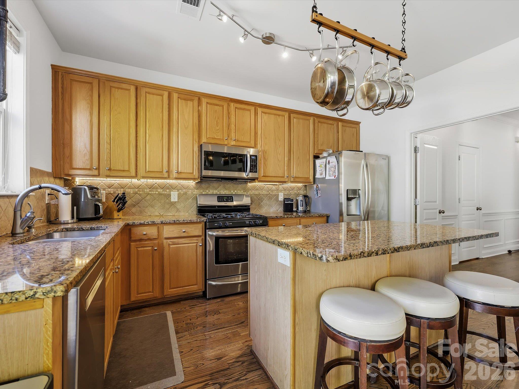The spacious kitchen features abundant cabinetry, granite countertops, stainless steel appliances, a tile backsplash, and a large center island with casual seating. - 11732 Windy Mist Way, Huntersville
