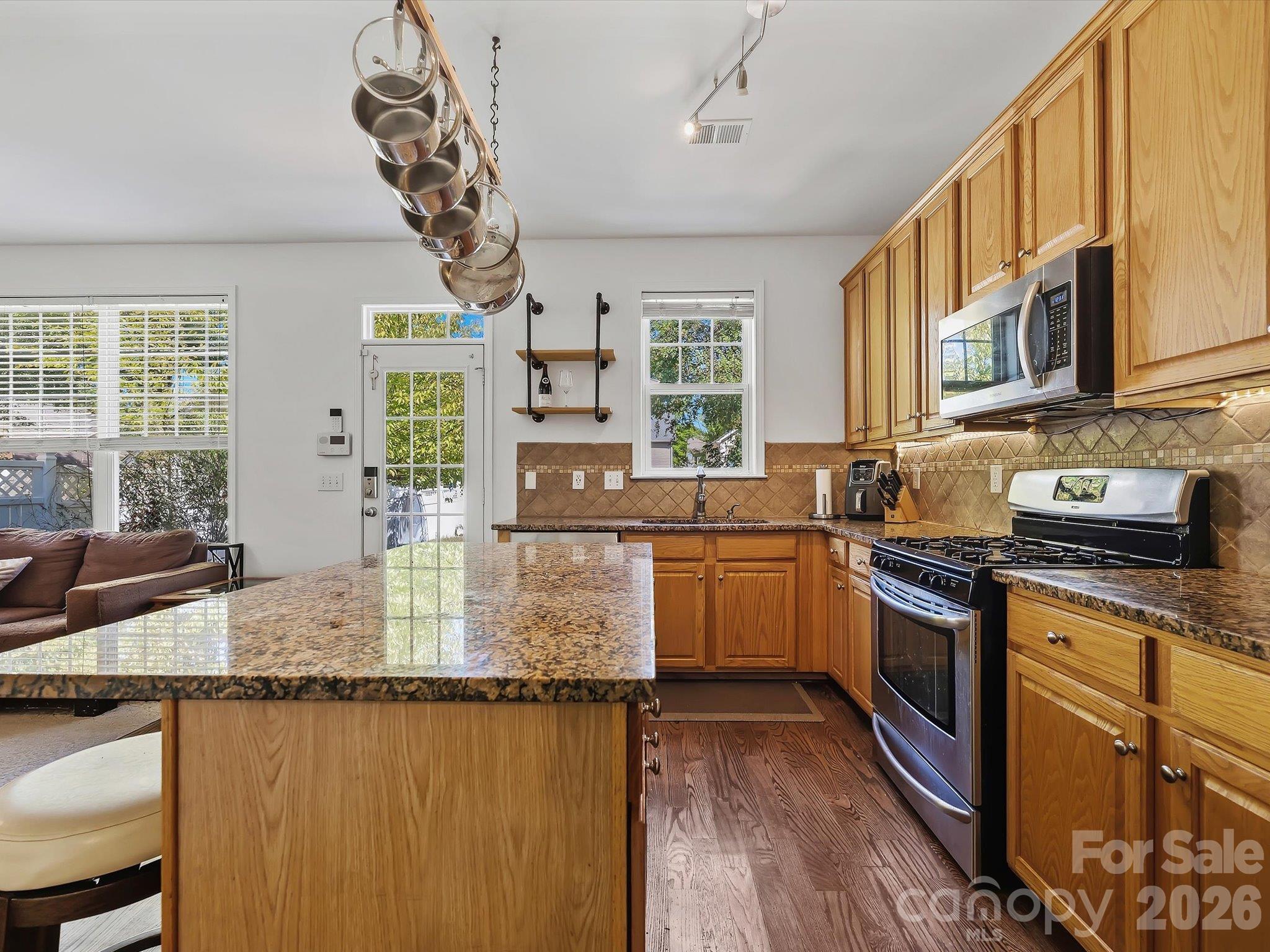 The spacious kitchen features abundant cabinetry, granite countertops, stainless steel appliances, a tile backsplash, and a large center island with casual seating. - 11732 Windy Mist Way, Huntersville