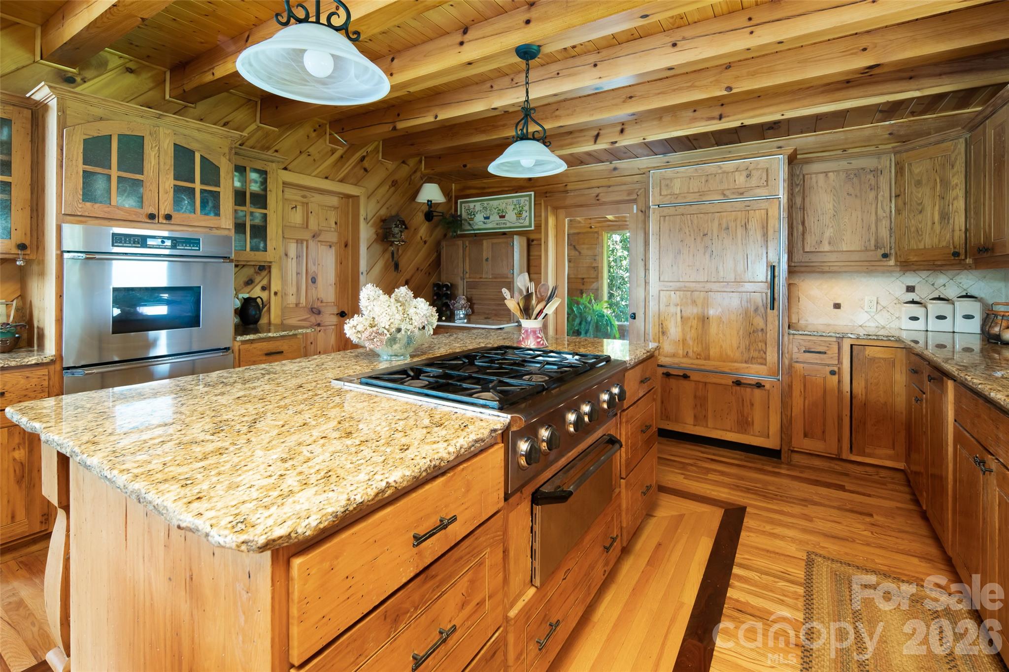 Granite kitchen countertops. Kitchen island with gas range. Double oven behind. Refrigerator at back center blends in with the cabinetry for a sleek, seamless look. - 316 Stevenson Cove Road, Waynesville