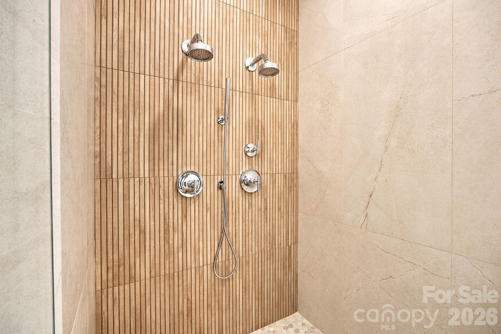 A luxurious primary walk-in shower featuring dual shower heads for an upscale, spa-like experience. - 18416 Peninsula Club Drive, Cornelius