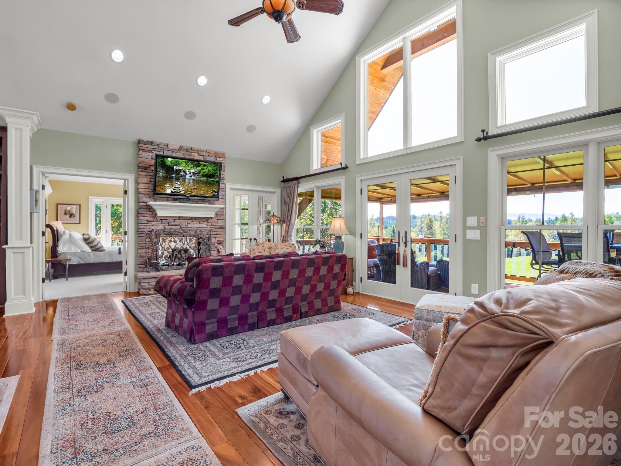 Gorgeous expansive windows and vaulted ceilings in the living room overlooking mountain views, see-through fireplace and looking into the primary bedroom on main - 140 Blazing Star Lane, Mill Spring