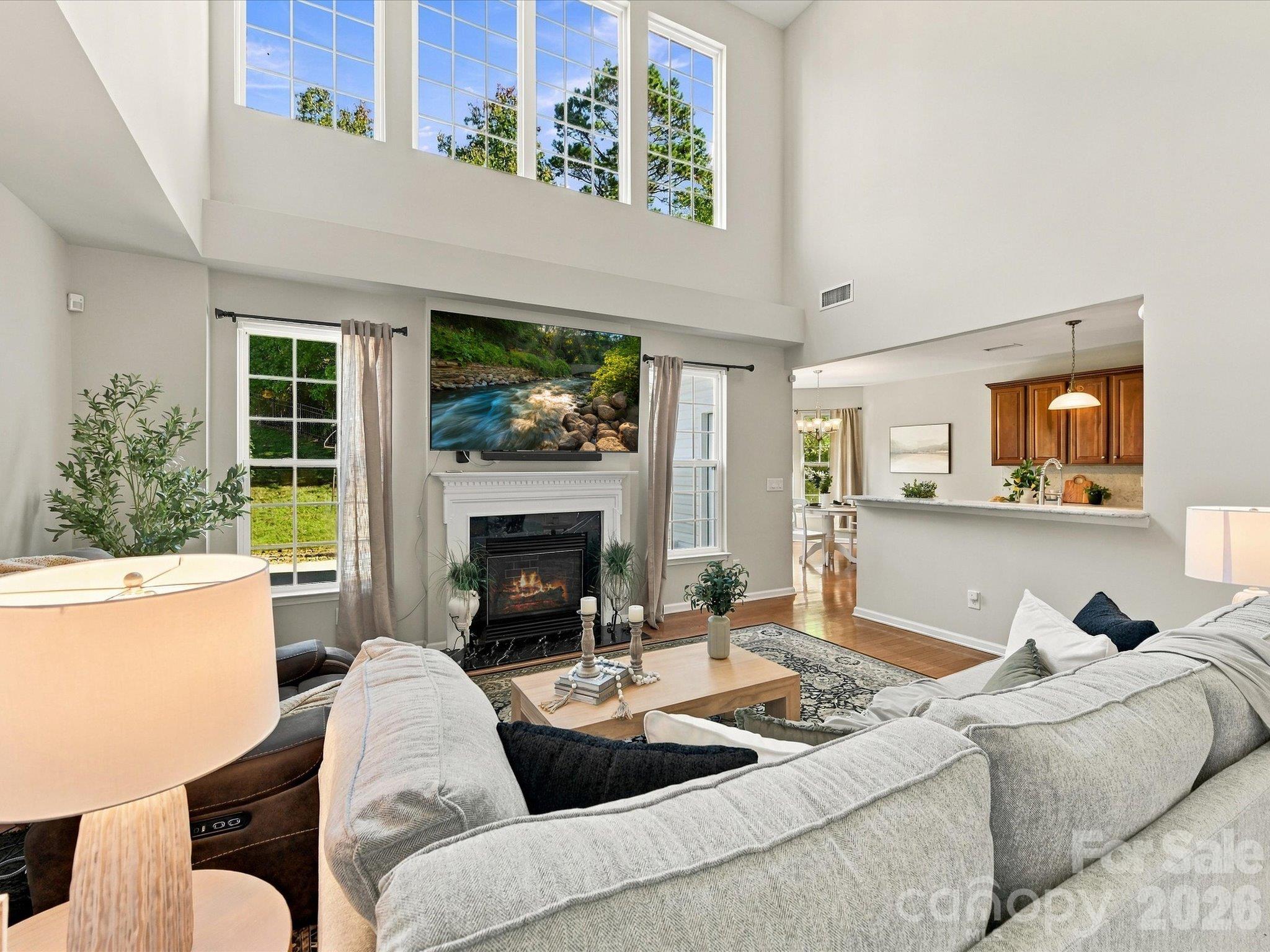 Light-filled living room featuring soaring ceilings, expansive windows, rich hardwood floors, and a cozy fireplace that creates a warm and inviting gathering space. - 1788 Oakmont Drive, Denver