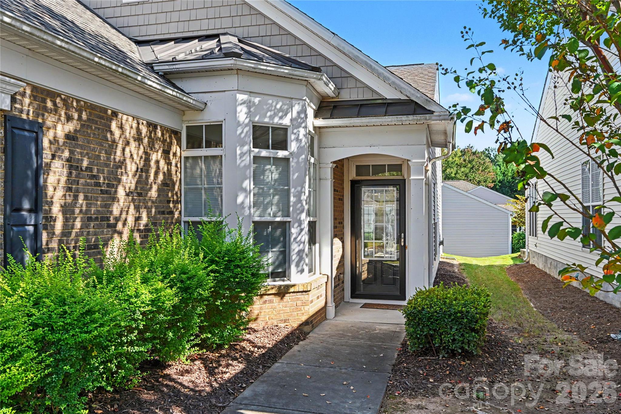 Front view showing front door with glass storm door, bay window area for Breakfast, brick front, and mature landscaping. - 3054 Azalea Drive, Indian Land