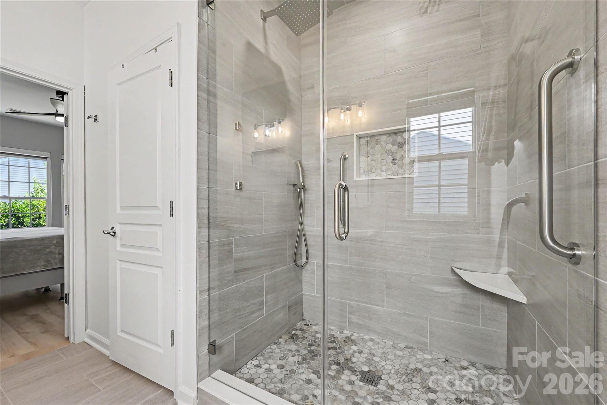 Another view of the LUXURIOUS SHOWER in the Primary Bath showing custom ceiling to floor tile, tile floor pan, frameless glass door and surround, body jets, Rain shower, and grab handle. - 3054 Azalea Drive, Indian Land