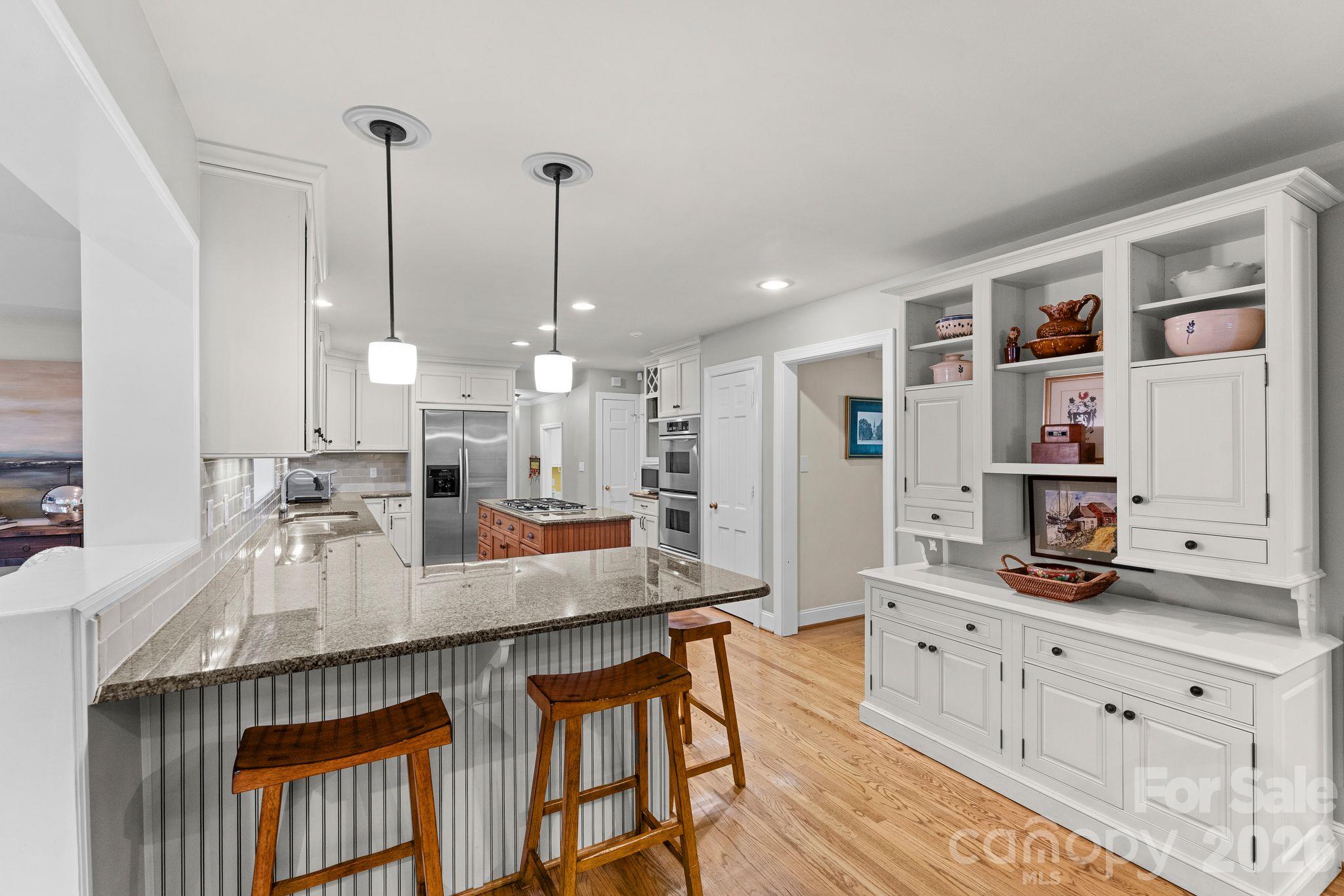 White kitchen cabinetry with pendant lights over bar seating - 2006 Grey Road, Davidson