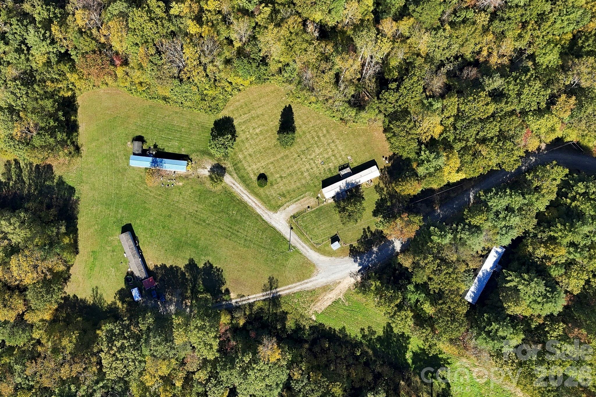 Bird's-eye view showcasing multiple mobile homes, established gravel driveways, and expansive open areas bordered by woodland. - 631 Union Hill Road, Hendersonville