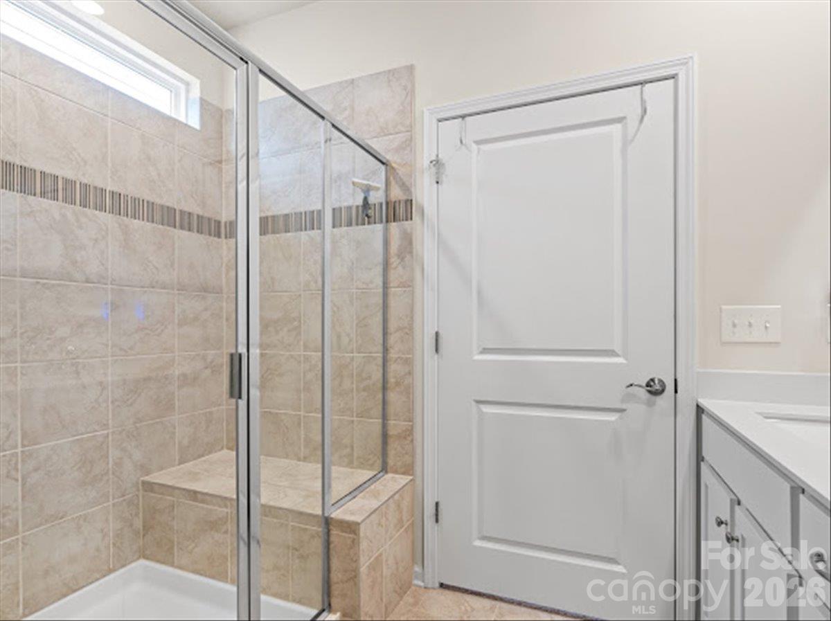 Beautiful glass-enclosed walk-in shower featuring bench, stunning neutral tilework in a modern, spa-like setting. - 155 White Apple Way, Statesville