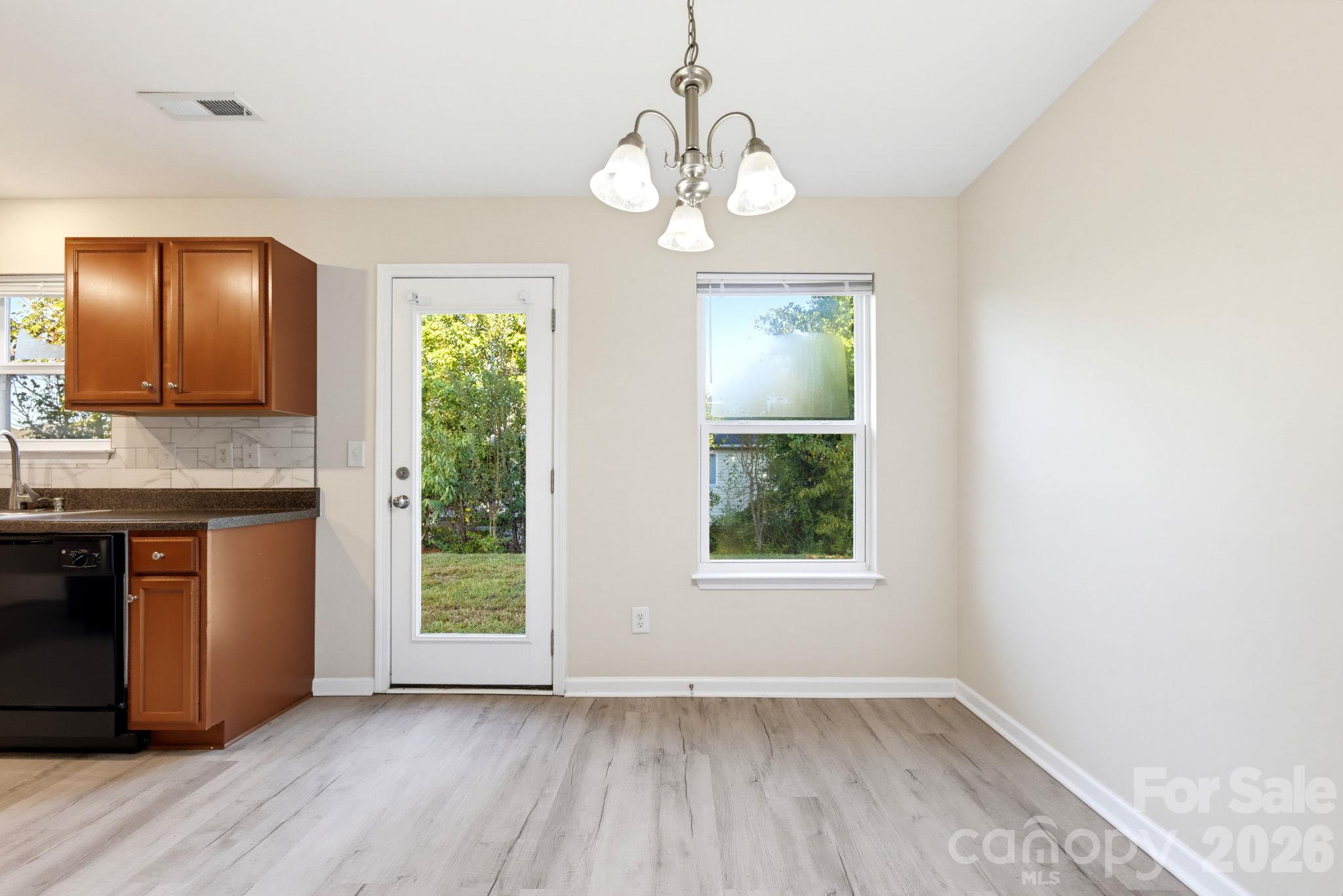Dining area with a statement light fixture, warm wood cabinetry, and convenient access to the backyard. - 5718 Natick Drive, Charlotte