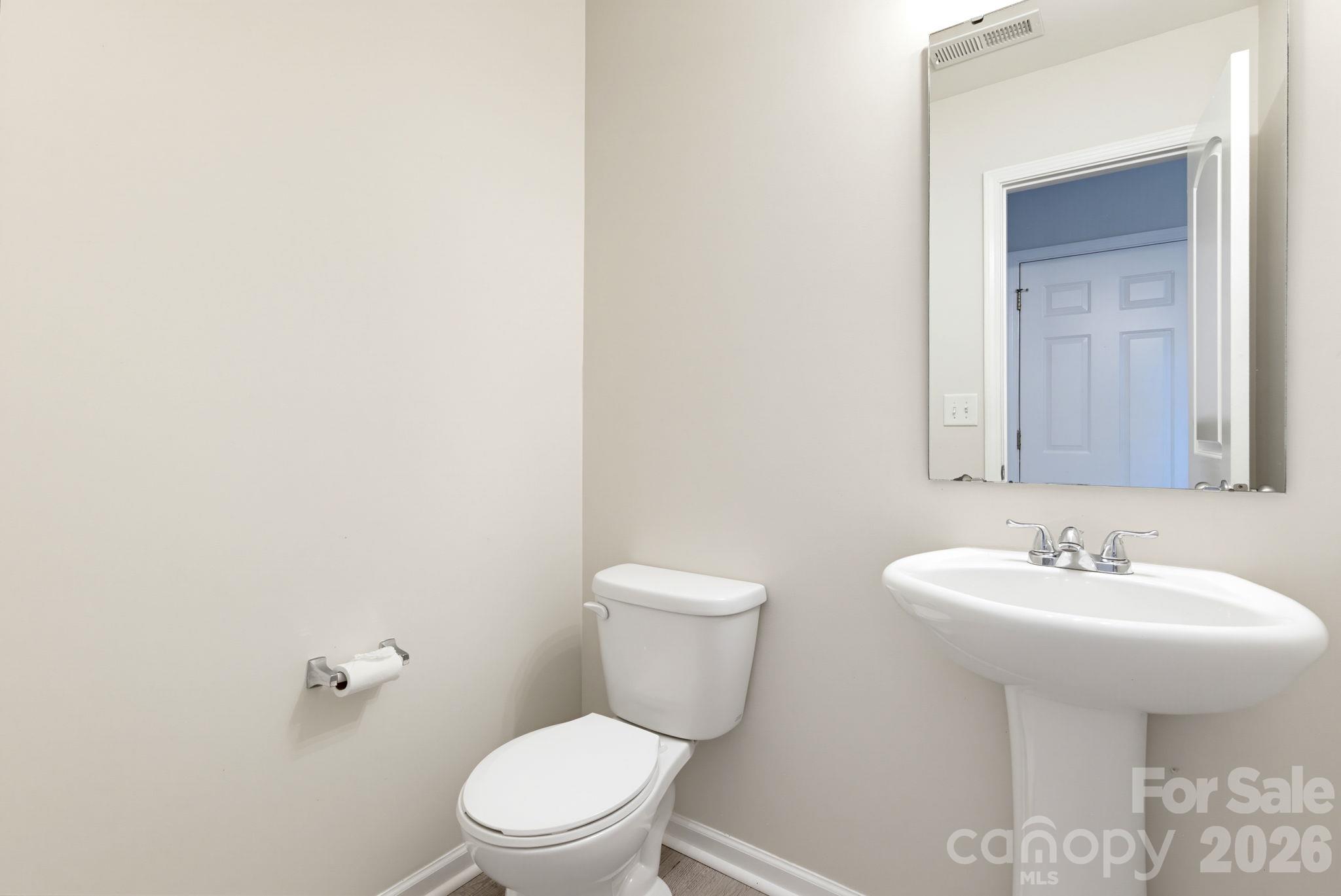 Convenient half bathroom featuring a pedestal sink, toilet, and neutral finishes. - 5718 Natick Drive, Charlotte