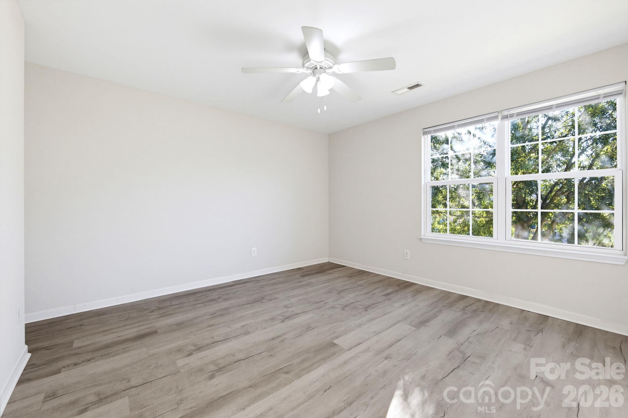 Spacious bedroom with a ceiling fan, large windows, and modern flooring. - 5718 Natick Drive, Charlotte