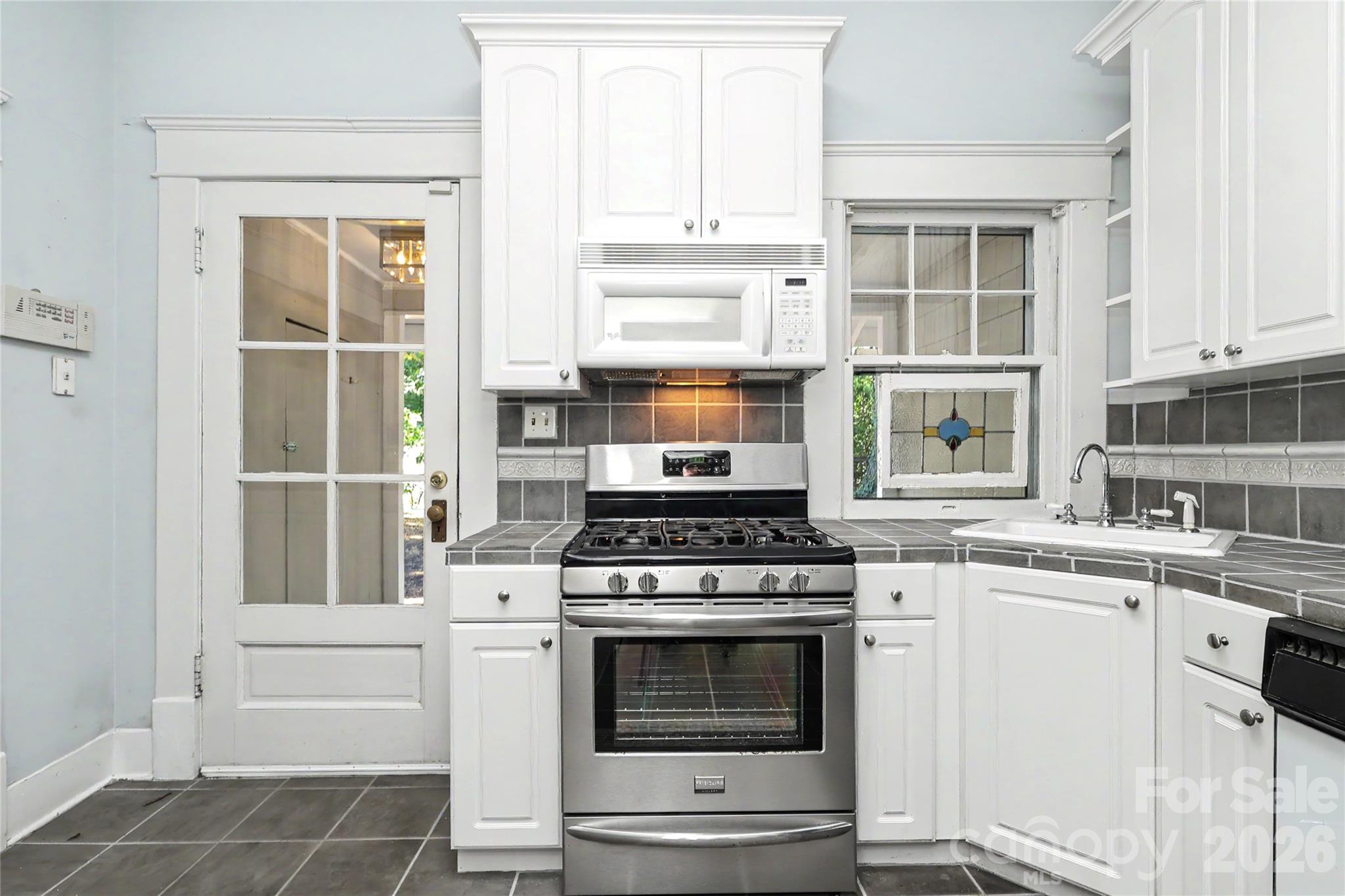Charming kitchen with stained glass window feature, gas range, great cabinet storage, tile accented countertops and flooring - 1933 Park Road, Charlotte