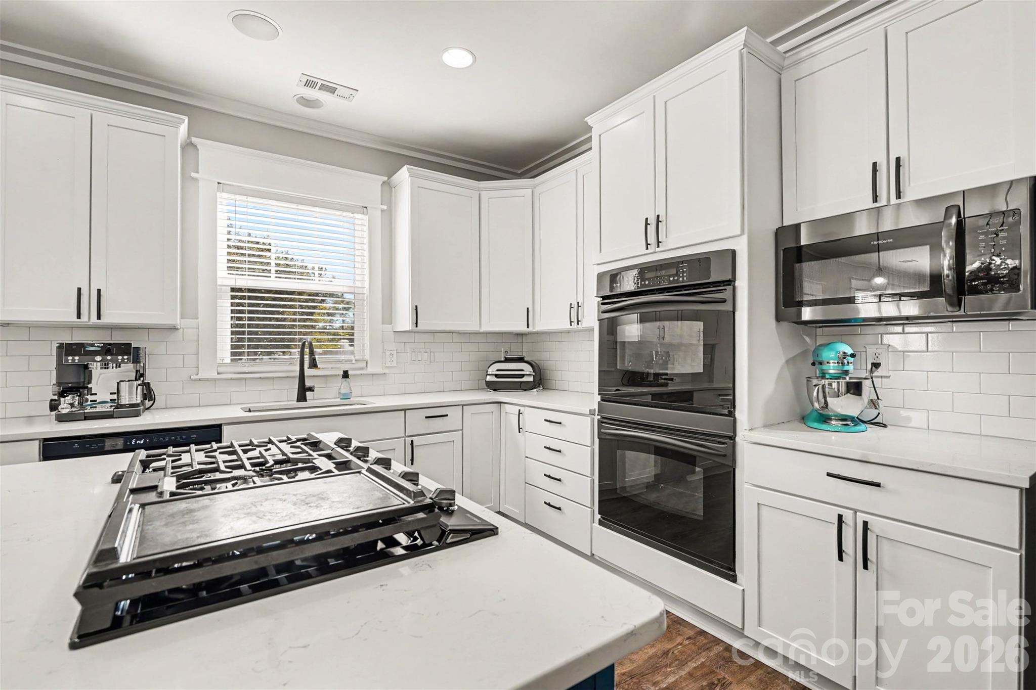 Love the sleek design of this kitchen. White cabinets, white subway tile backsplash, built-in double ovens, built-in Gas cooktop. Love the window above the sink! - 3585 Leighton Drive SW, Concord