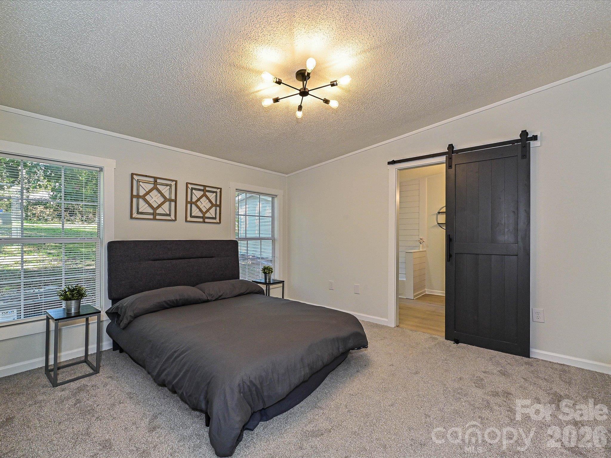 View of primary suite with barn door entrance to primary en-suite bathroom. Fresh new carpet provides a cozy place to relax. - 1711 Trexlar Avenue, Gastonia