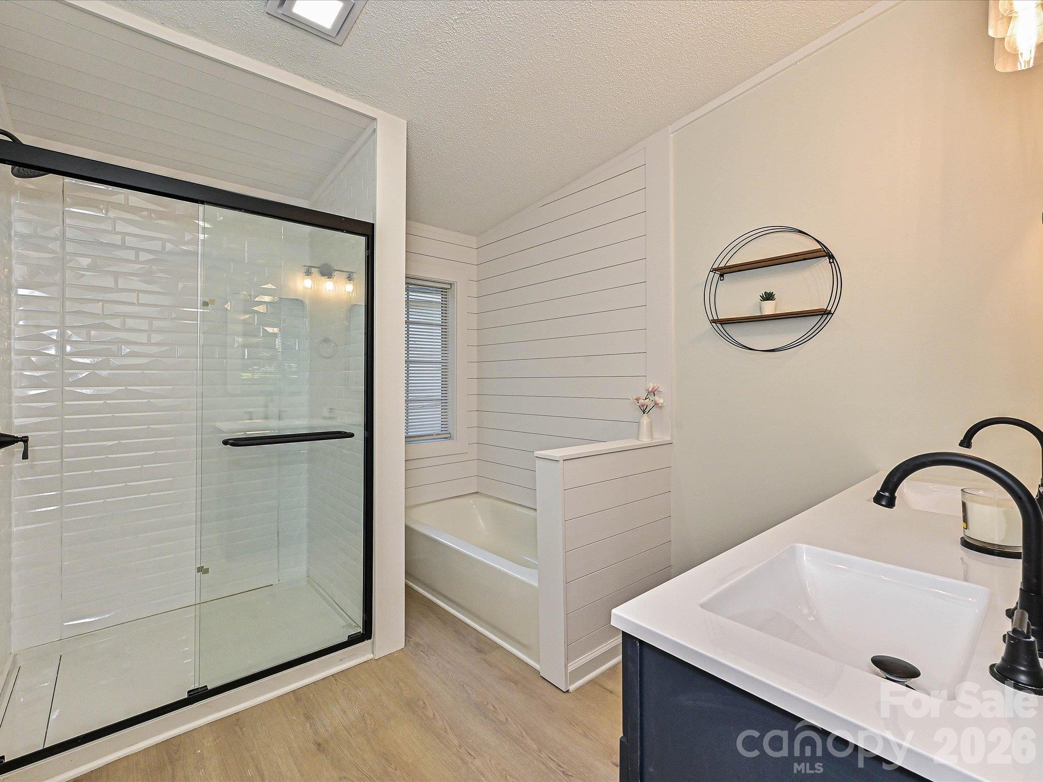 Beautiful primary suite with bathtub with shiplap surround, large walk-in shower with matte black shower door hardware, subway tile decor surround and new double vanity. - 1711 Trexlar Avenue, Gastonia