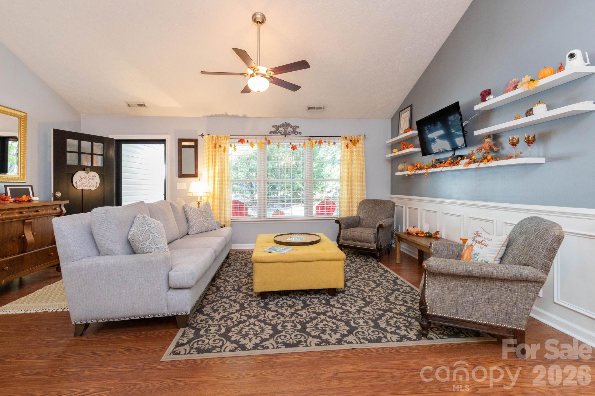 Welcoming living room featuring a vaulted ceiling, wood flooring, decorative wall paneling, and a large window overlooking the front porch. - 139 Lone Eagle Lane, Hendersonville