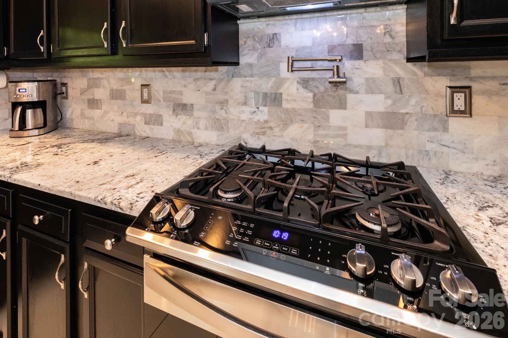 Kitchen detail showcasing the gas range, pot-filler faucet, tile backsplash, and surrounding counter space. - 139 Lone Eagle Lane, Hendersonville