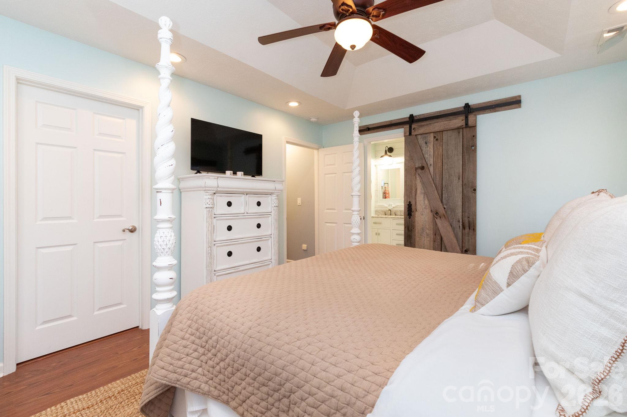 Primary bedroom view highlighting the tray ceiling, wood flooring, and rustic sliding barn door. - 139 Lone Eagle Lane, Hendersonville