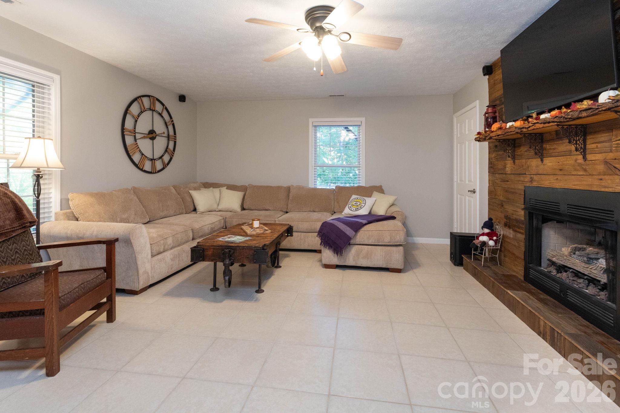 Comfortable additional living area featuring tile flooring, a ceiling fan, and a fireplace framed by a wood accent wall. - 139 Lone Eagle Lane, Hendersonville