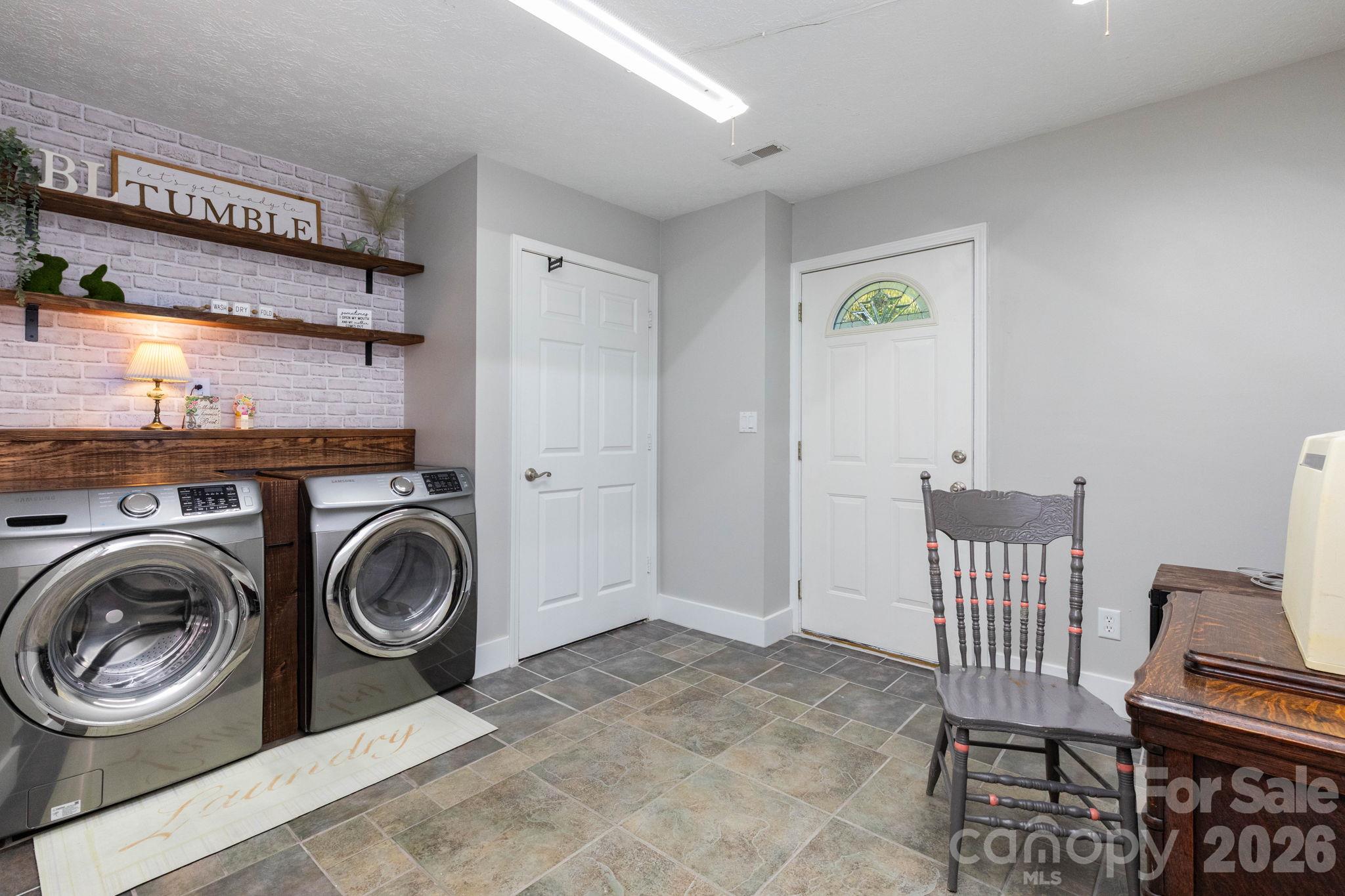 Laundry room with side-by-side washer and dryer space, open shelving, a folding counter, and an exterior entry door. - 139 Lone Eagle Lane, Hendersonville