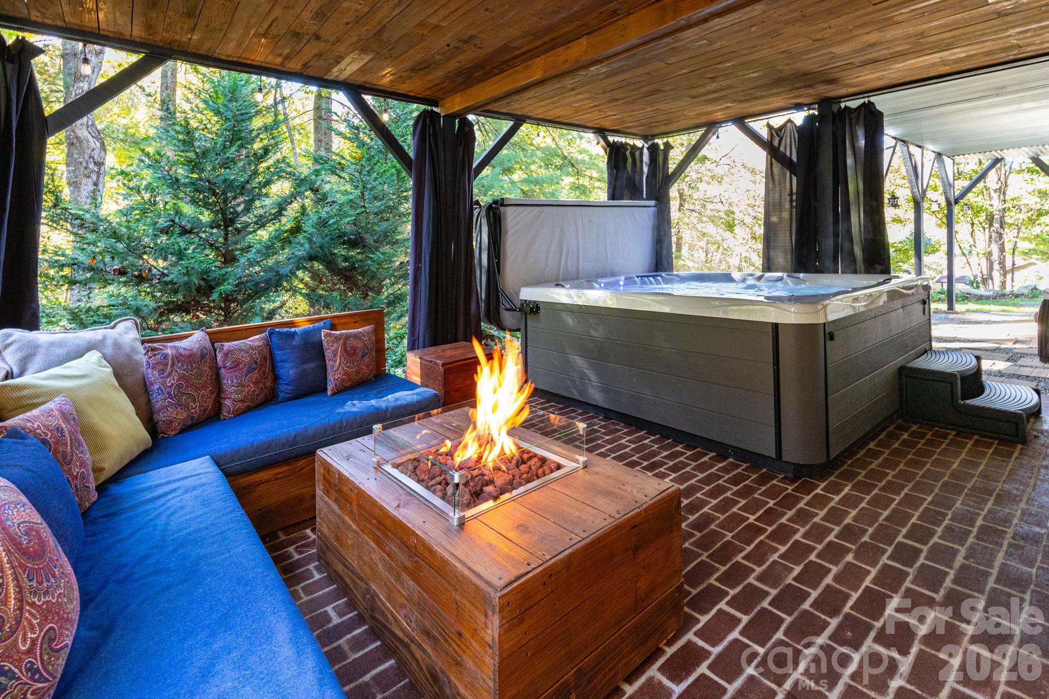 Covered outdoor retreat featuring a hot tub, lounge seating, a fire table, and a wood ceiling overlooking the surrounding greenery. - 139 Lone Eagle Lane, Hendersonville