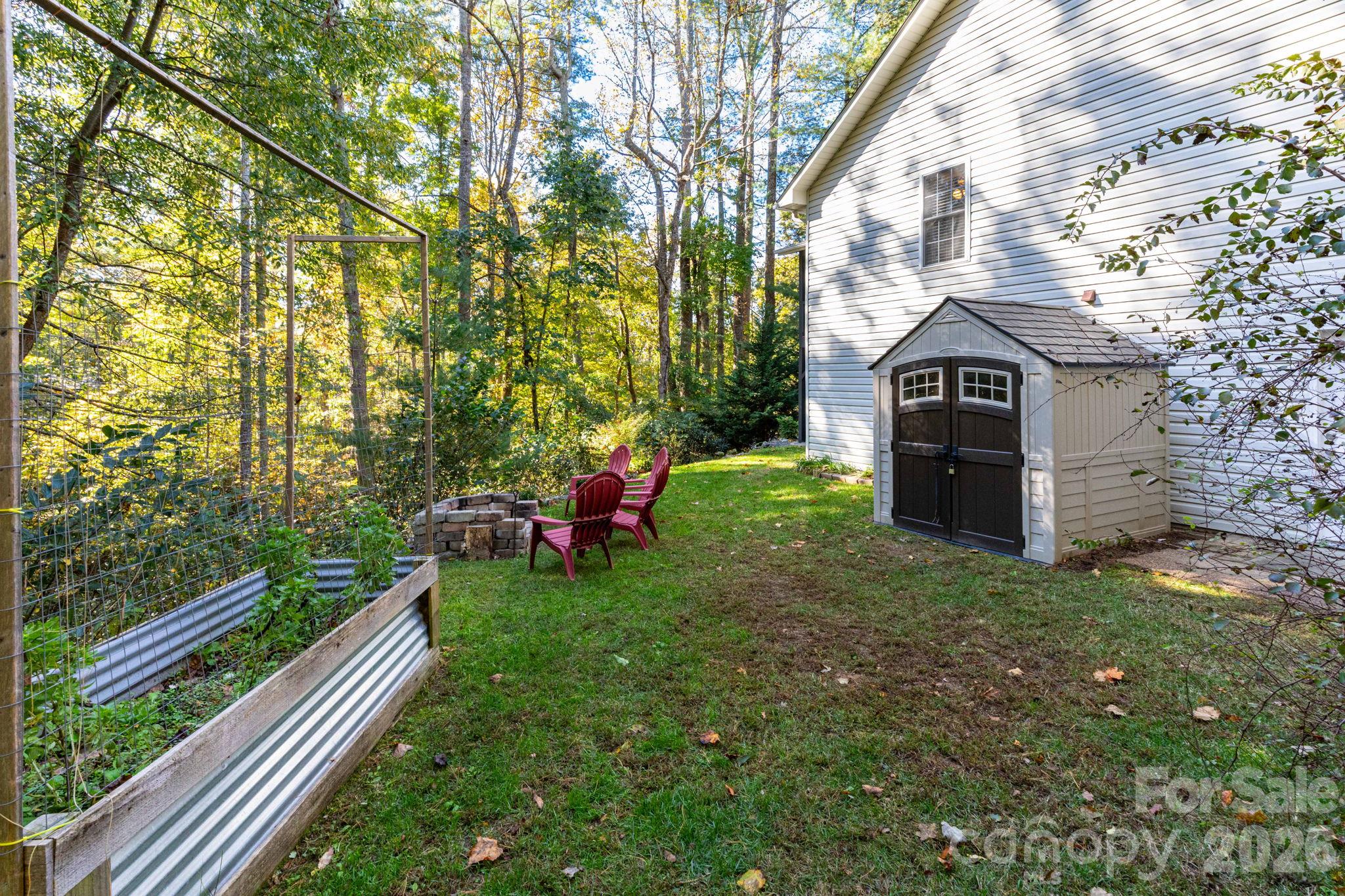 Outdoor area featuring raised garden beds, a storage shed, and space for seating beside the wooded surroundings. - 139 Lone Eagle Lane, Hendersonville