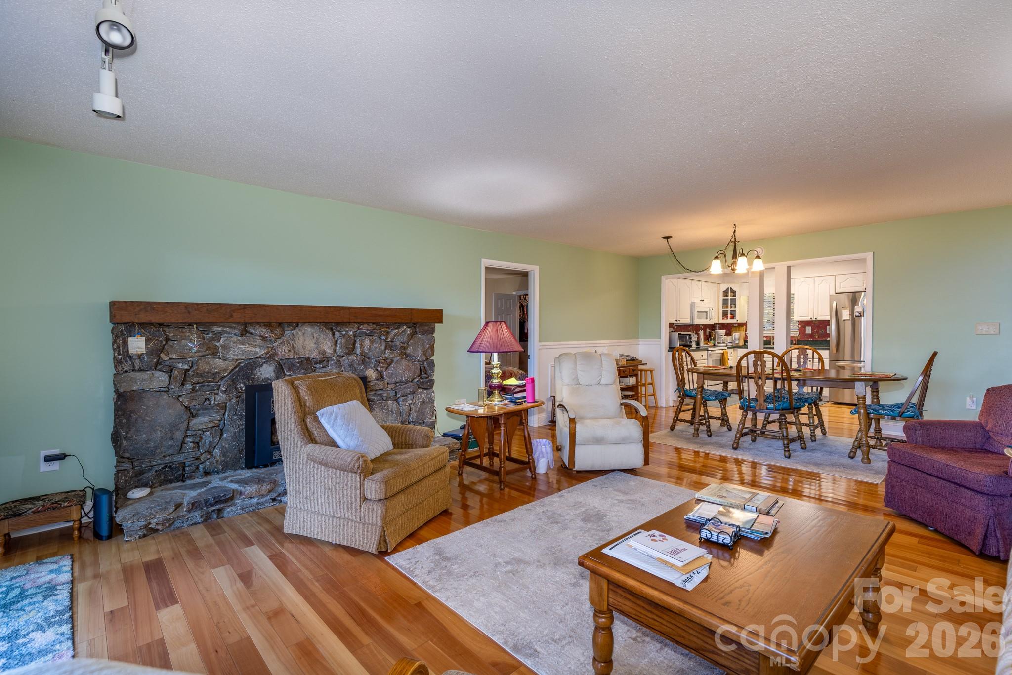 Spacious living room featuring beautiful hardwood floors, a native stone fireplace with gas-log insert, and an open layout connecting the living, dining, and kitchen areas. - 524 Three Mile Knob Road, Pisgah Forest