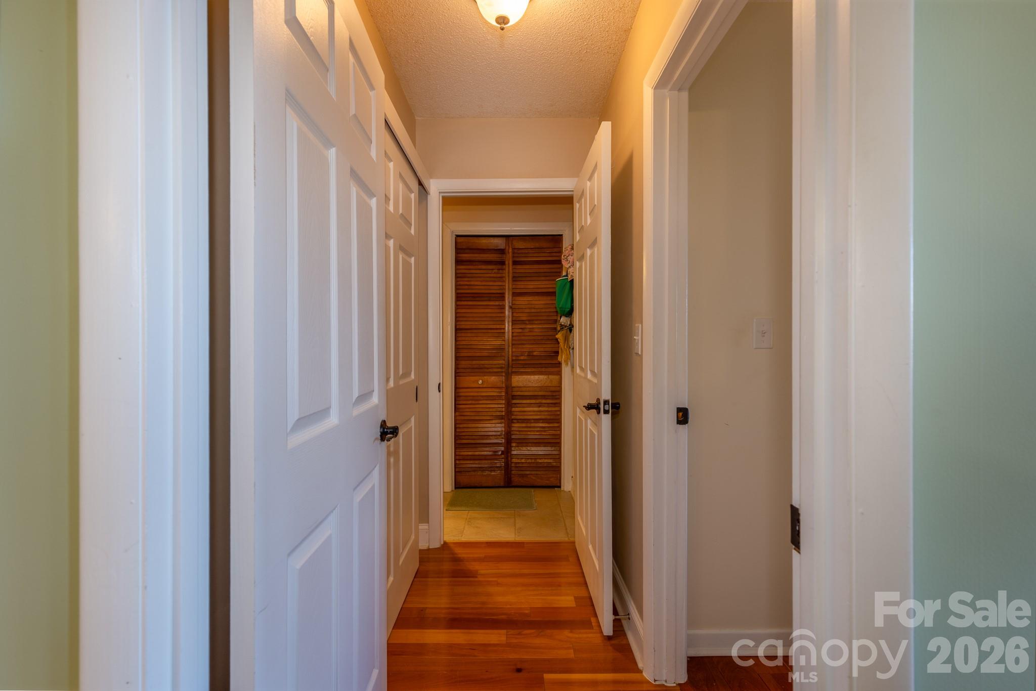Interior hallway with hardwood flooring, multiple storage closets, and convenient access to the bedrooms and bathrooms. - 524 Three Mile Knob Road, Pisgah Forest