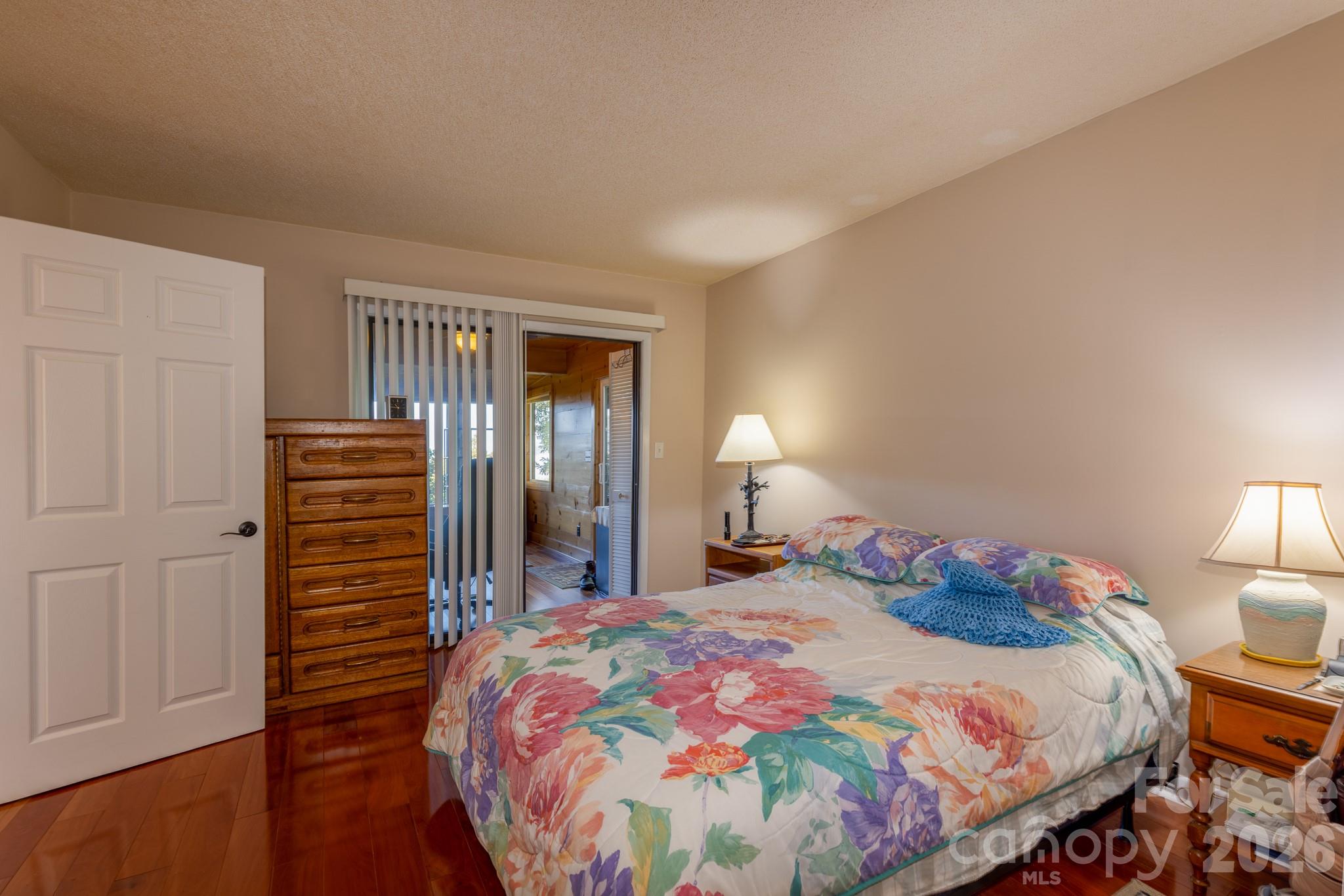 Another view of the primary bedroom highlighting beautiful hardwood floors and sliding glass doors leading into the wood-paneled sunroom. - 524 Three Mile Knob Road, Pisgah Forest