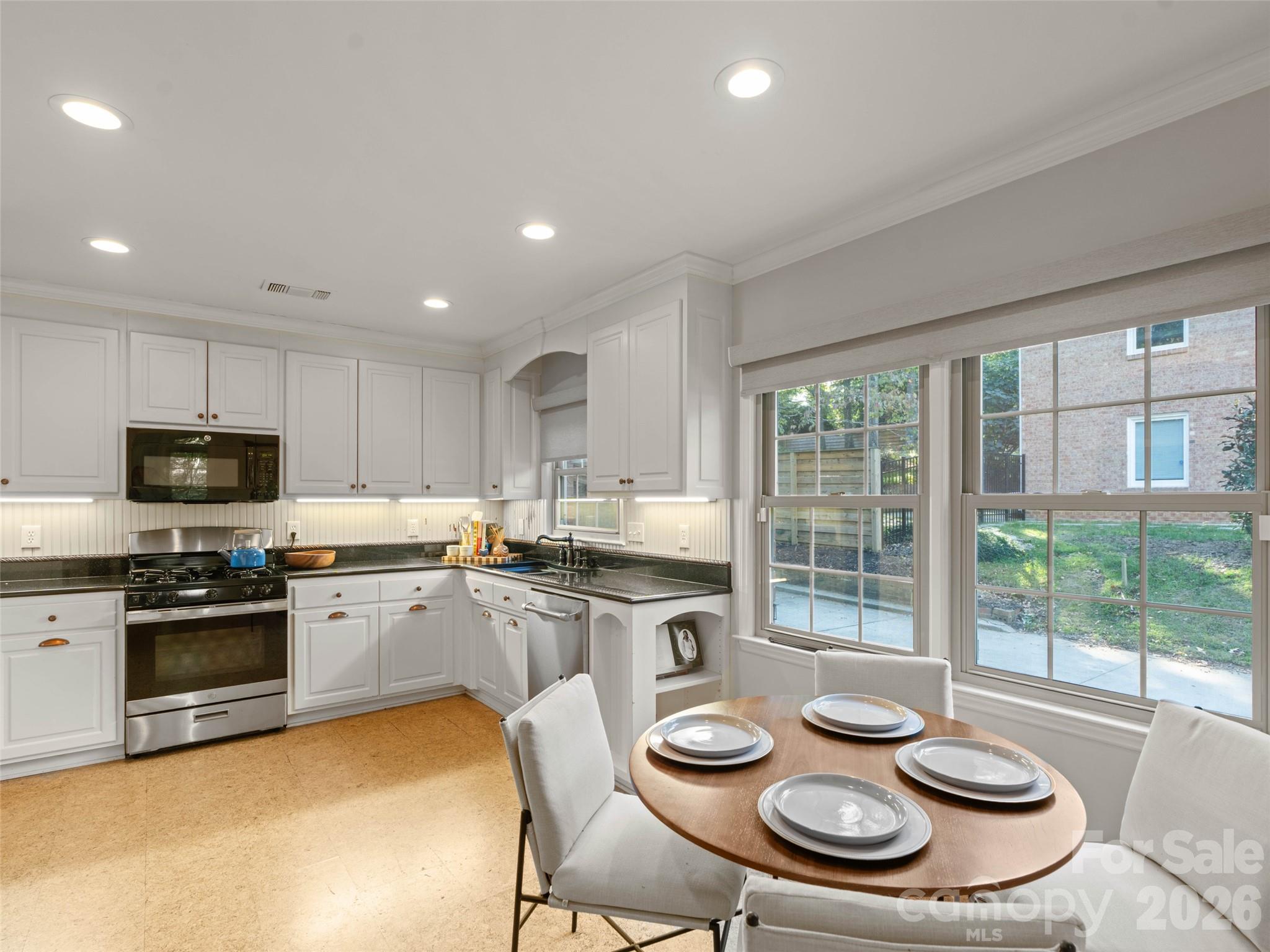 Bright and inviting kitchen featuring painted cabinetry, granite countertops, and newer appliances. Cork flooring adds warmth and character, while the cozy eat-in area provides the perfect spot for casual dining and everyday gatherings. - 6626 Rocky Falls Road, Charlotte