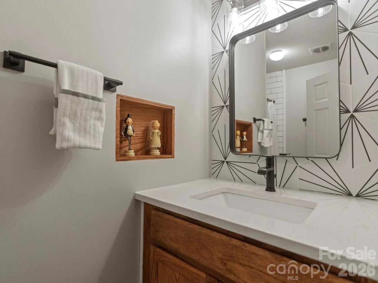 The main-level hallway bathroom has been tastefully updated with a refreshed vanity, modern mirror, updated faucet, and stylish tile backsplash, creating a clean and contemporary look. - 6626 Rocky Falls Road, Charlotte