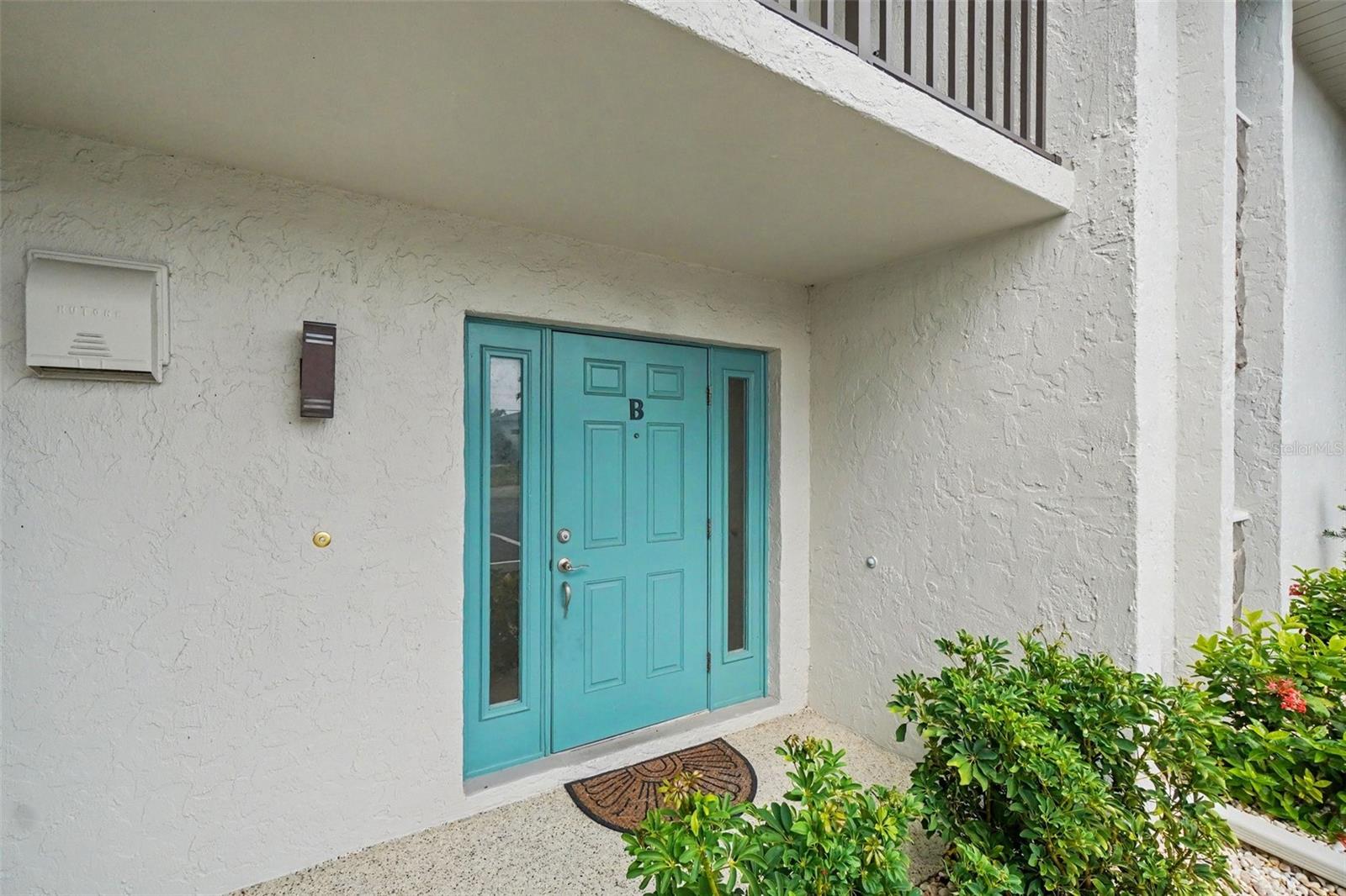 Front entry to unit B with a turquoise front door, covered walkway, and tropical landscaping at this Punta Gorda waterfront condo. - 1423 MEDITERRANEAN DR #B, PUNTA GORDA