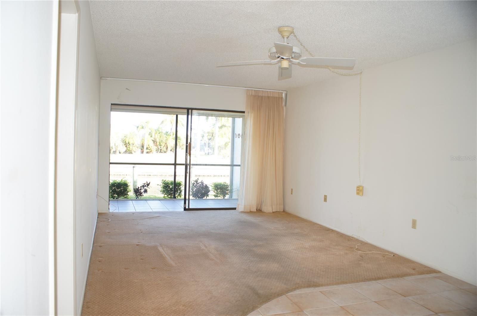 Living room with sliding glass doors opening to the screened lanai, ceiling fan, and natural light from the canal side of the condo. - 1423 MEDITERRANEAN DR #B, PUNTA GORDA