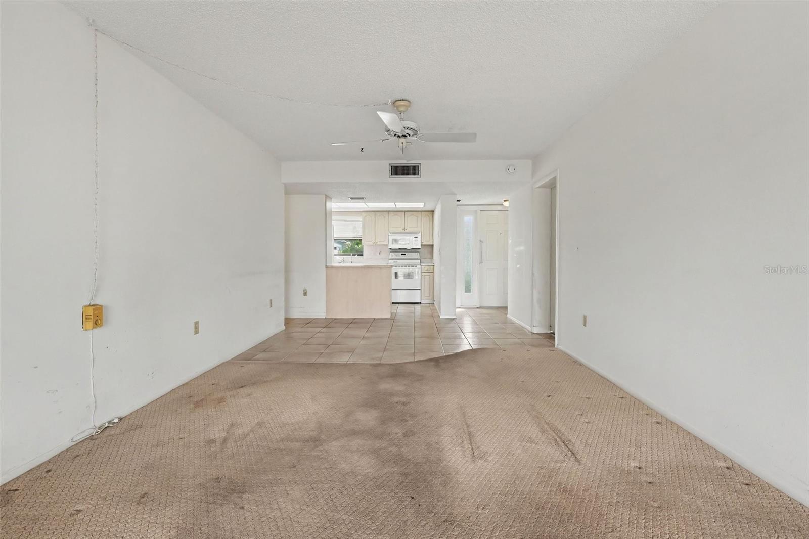 Open living and dining area looking toward the kitchen and front entry, with ceiling fan and tile flooring in the entry and kitchen. - 1423 MEDITERRANEAN DR #B, PUNTA GORDA