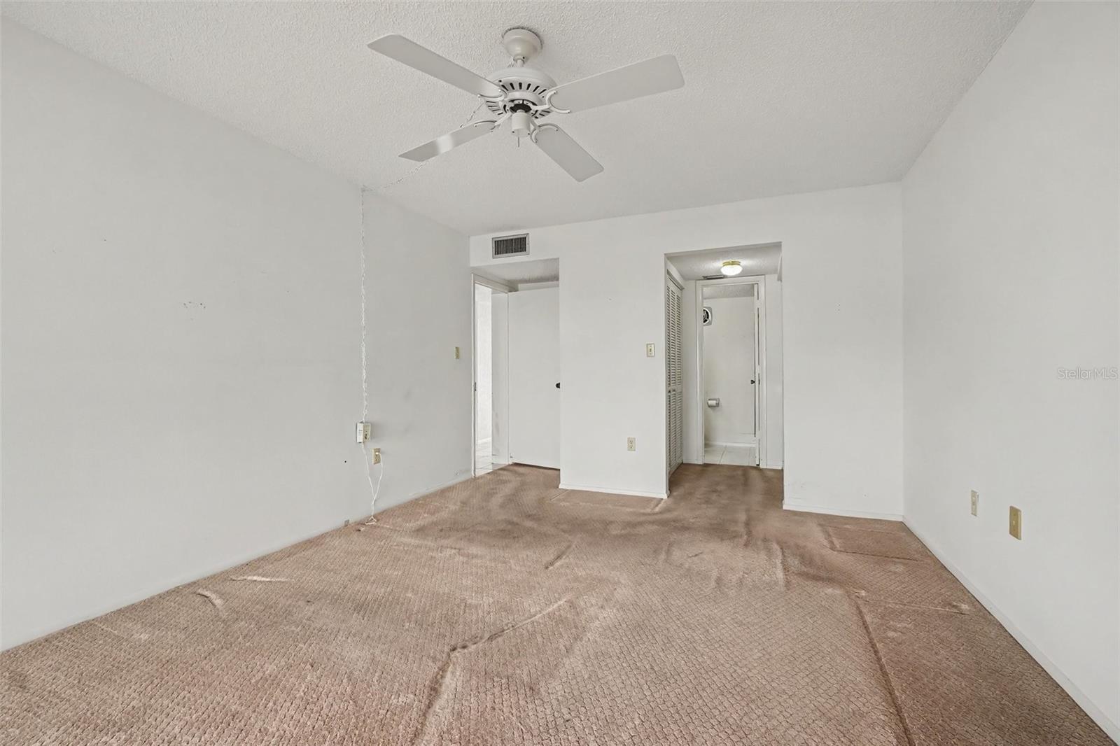 Primary bedroom with ceiling fan, carpet, and direct access to the en-suite bathroom. - 1423 MEDITERRANEAN DR #B, PUNTA GORDA