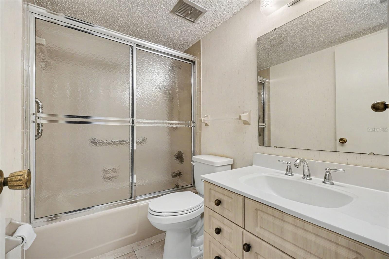 Guest bathroom with tub and shower combination behind glass sliding doors, single vanity with storage, and wide mirror. - 1423 MEDITERRANEAN DR #B, PUNTA GORDA