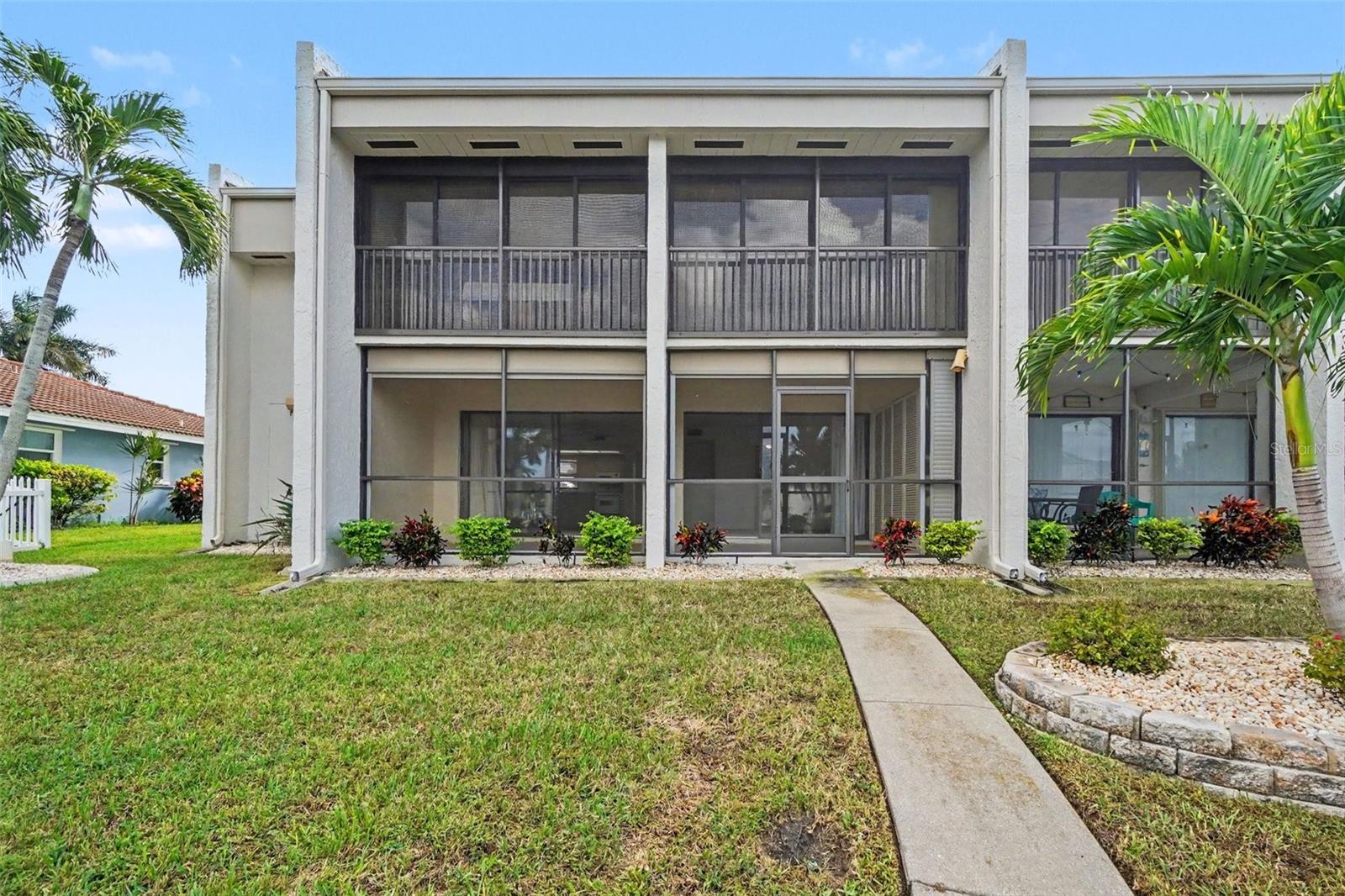 Rear view of the first-floor condo with screened lanai and a walkway across the lawn leading to the private dock. - 1423 MEDITERRANEAN DR #B, PUNTA GORDA