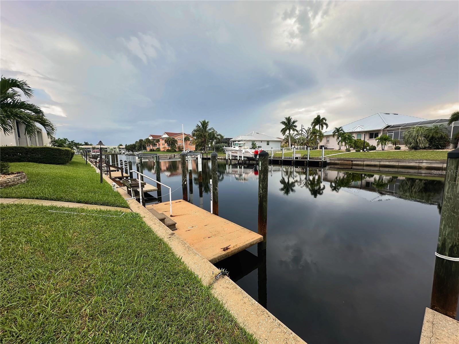 View from the dock down the Punta Gorda canal, with the lawn and seawall behind the first-floor condo. - 1423 MEDITERRANEAN DR #B, PUNTA GORDA