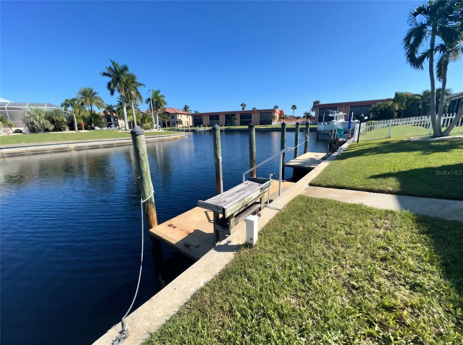 Deeded boat dock at 1423 Mediterranean Dr on a Punta Gorda canal, with dock box, pilings, and steps from the lawn to the water. - 1423 MEDITERRANEAN DR #B, PUNTA GORDA