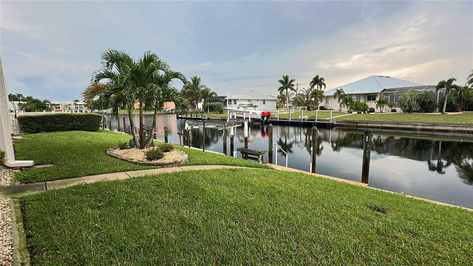 Waterfront lawn with palm landscaping along the canal behind the condo, a short walk to the dock. - 1423 MEDITERRANEAN DR #B, PUNTA GORDA