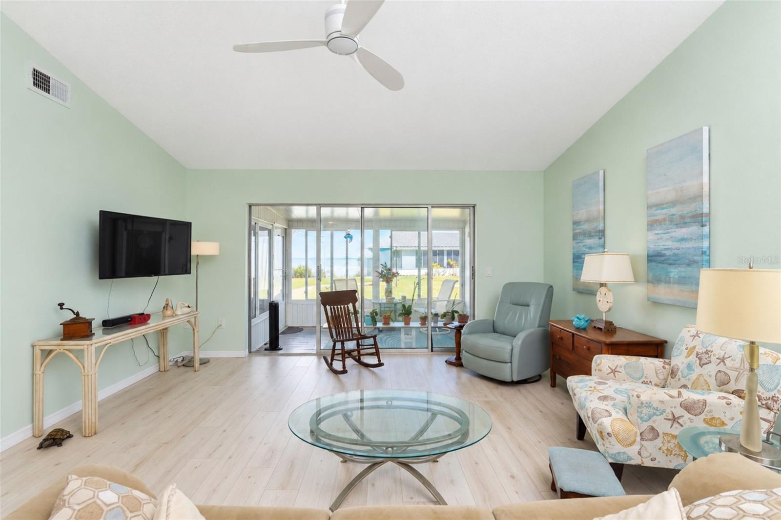 The living room has stylish wood laminate flooring, a ceiling fan and sliding glass doors to the Glass-Enclosed Florida room. - 6468 HAMLET DR #B, ENGLEWOOD