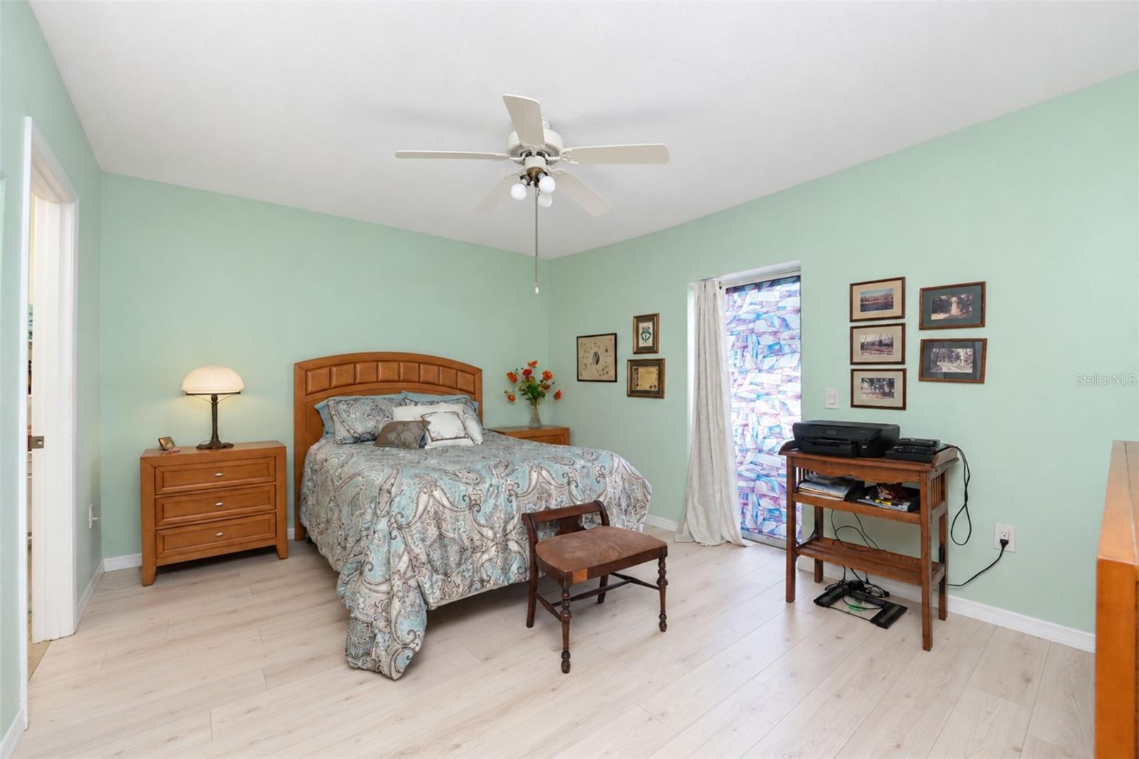 The primary bedroom features wood laminate flooring, a ceiling fan and sliding glass doors to the rear patio. - 6468 HAMLET DR #B, ENGLEWOOD