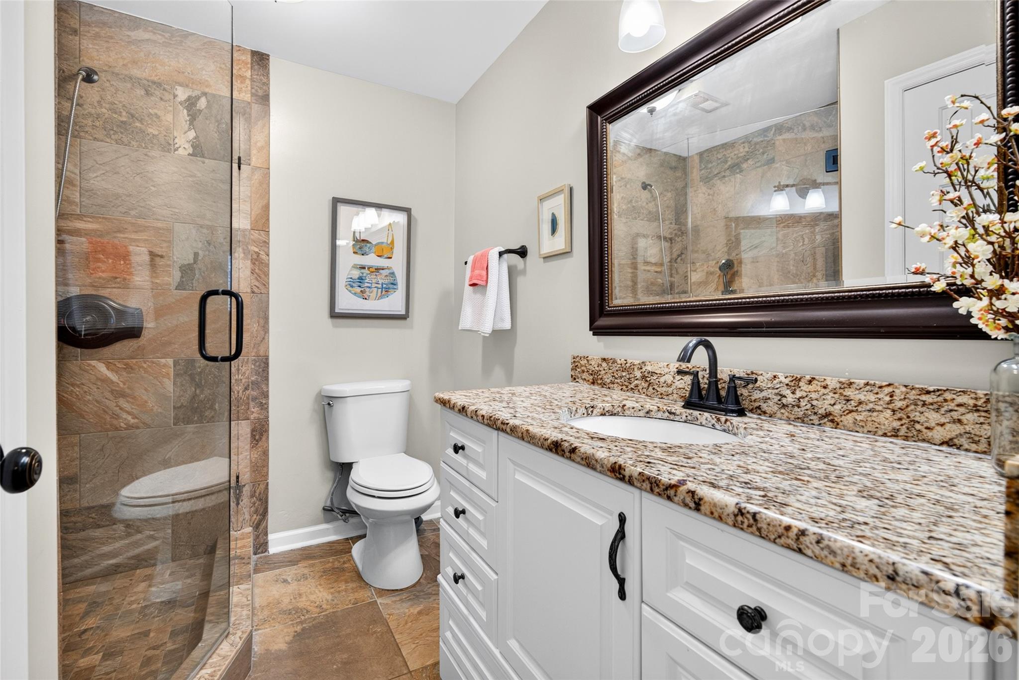 Beautiful primary bathroom featuring gorgeous granite countertops, tile flooring, and a tiled shower with glass enclosure! - 928 Southwest Drive, Davidson