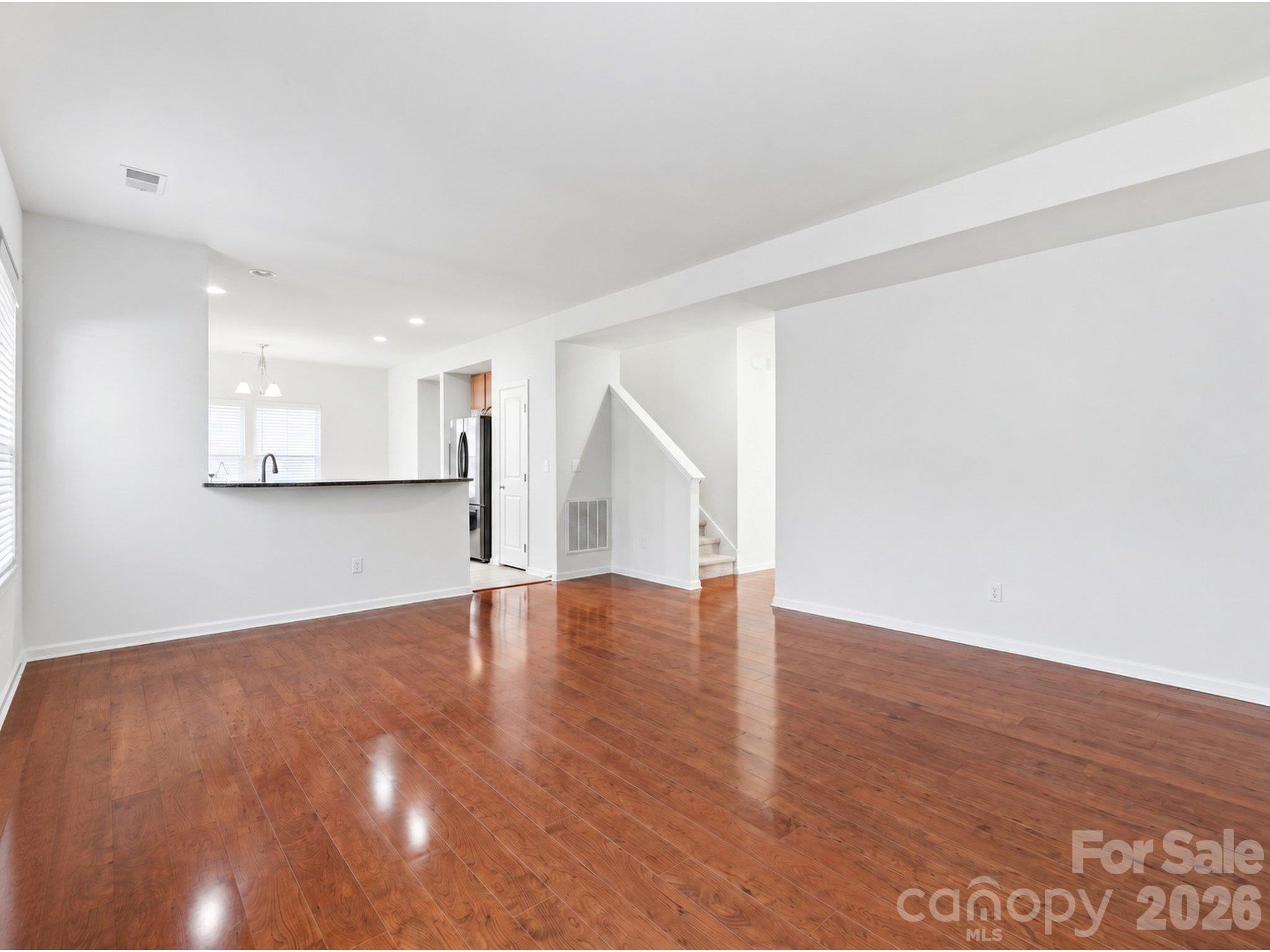 Living room: Unstaged view showing wood flooring, generous wall space for furniture placement, and the raised breakfast bar adjoining the kitchen. - 3341 Linetender Drive, Davidson