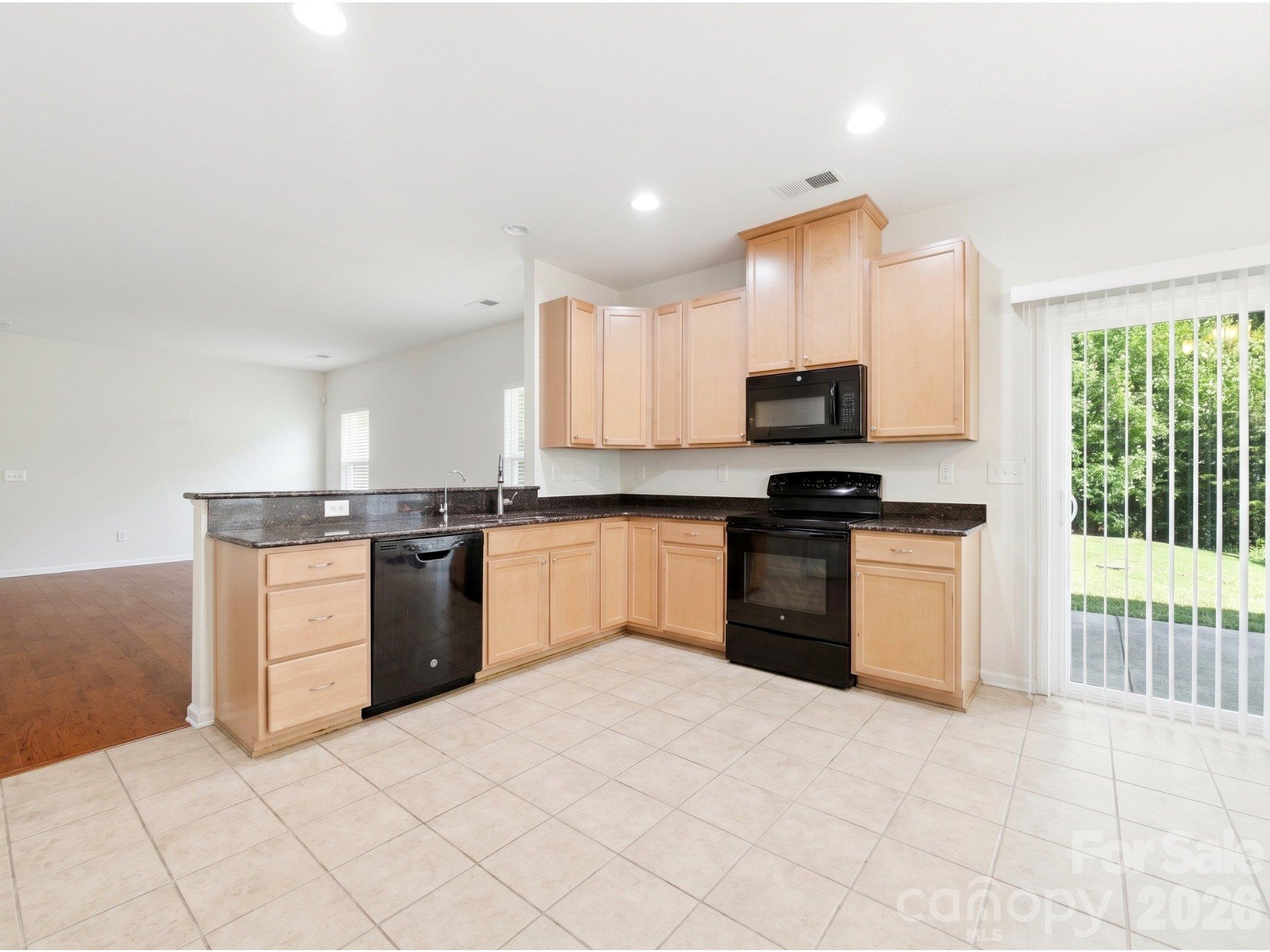 Kitchen: Granite countertops, maple cabinetry, recessed lighting, and a raised breakfast bar provide workspace and storage. Sliding doors lead to the backyard patio. - 3341 Linetender Drive, Davidson