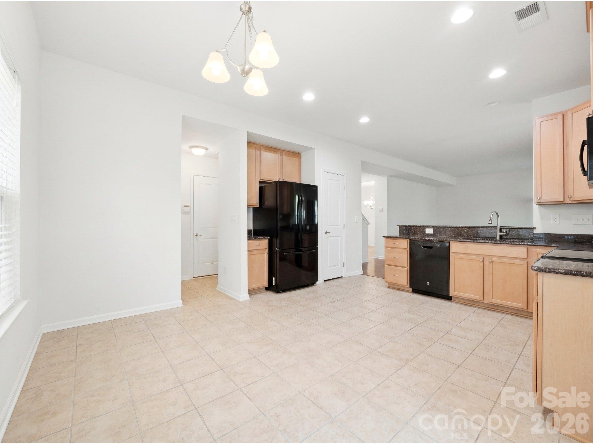 Kitchen and casual dining: Unstaged view showing cabinet storage, black appliances, and space for a dining table beside the sliding doors to the patio. - 3341 Linetender Drive, Davidson